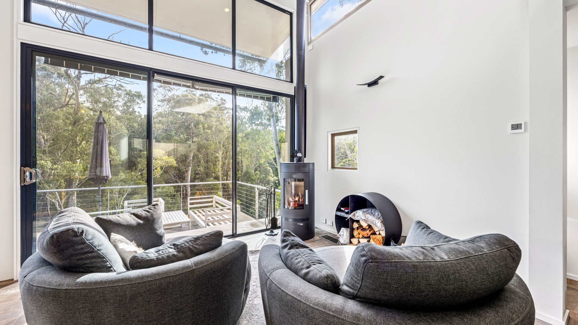 Een moderne woonkamer met een grote glazen deur die uitkomt op een balkon, een open haard en grijze gestoffeerde zithoek.