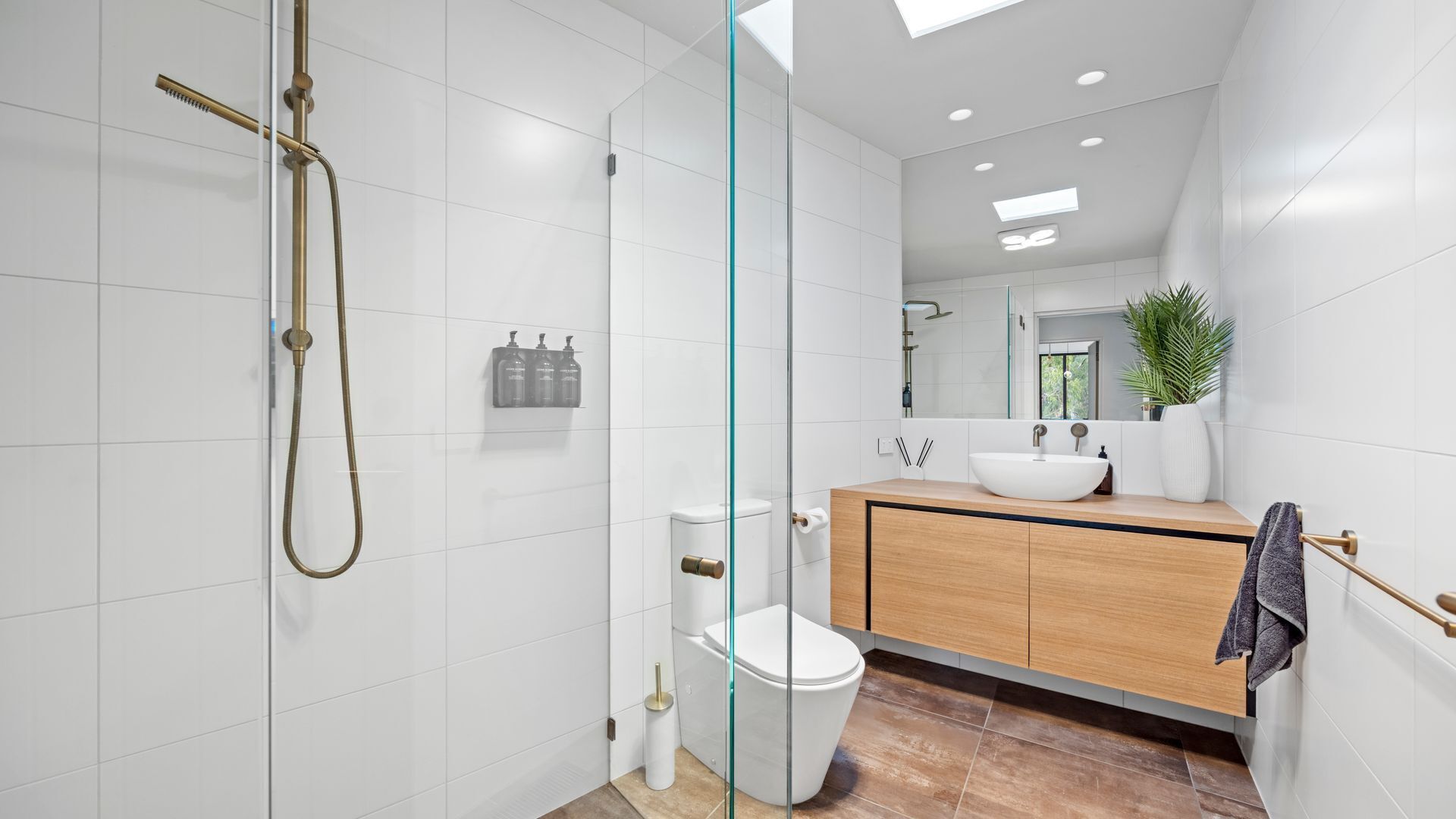A modern bathroom with a glass shower enclosure, a white toilet, a wooden vanity with a white sink, and a mirror above the sink.