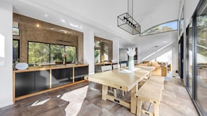 A modern kitchen with a large island, dark cabinetry, and a dining area with a wooden table and benches. - Riverfront Alpine Retreat - Mt Buller Gateway - Sleeps 10 (Merrijig)