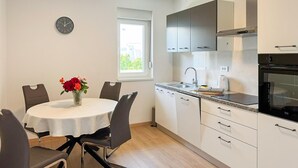 Una cocina moderna con armarios blancos, un horno de acero inoxidable y una zona de comedor con una mesa redonda y sillas.