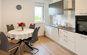 A modern kitchen with white cabinets, a stainless steel oven, and a dining area with a round table and chairs. - 1 bedroom lovely apartment in Kastel Stafilic (Kastel Stafilic)
