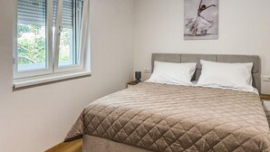 Un dormitorio con cama, una ventana con persianas, una mesita de noche y una lámpara de pared.
