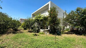 Un edificio moderno con techo plano, rodeado por un jardín con diversos árboles y arbustos.