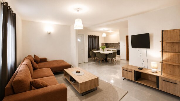 Ein modernes Wohnzimmer mit einem braunen Sofa, einem Holztisch, einem Fernseher und einem Essbereich im Hintergrund.