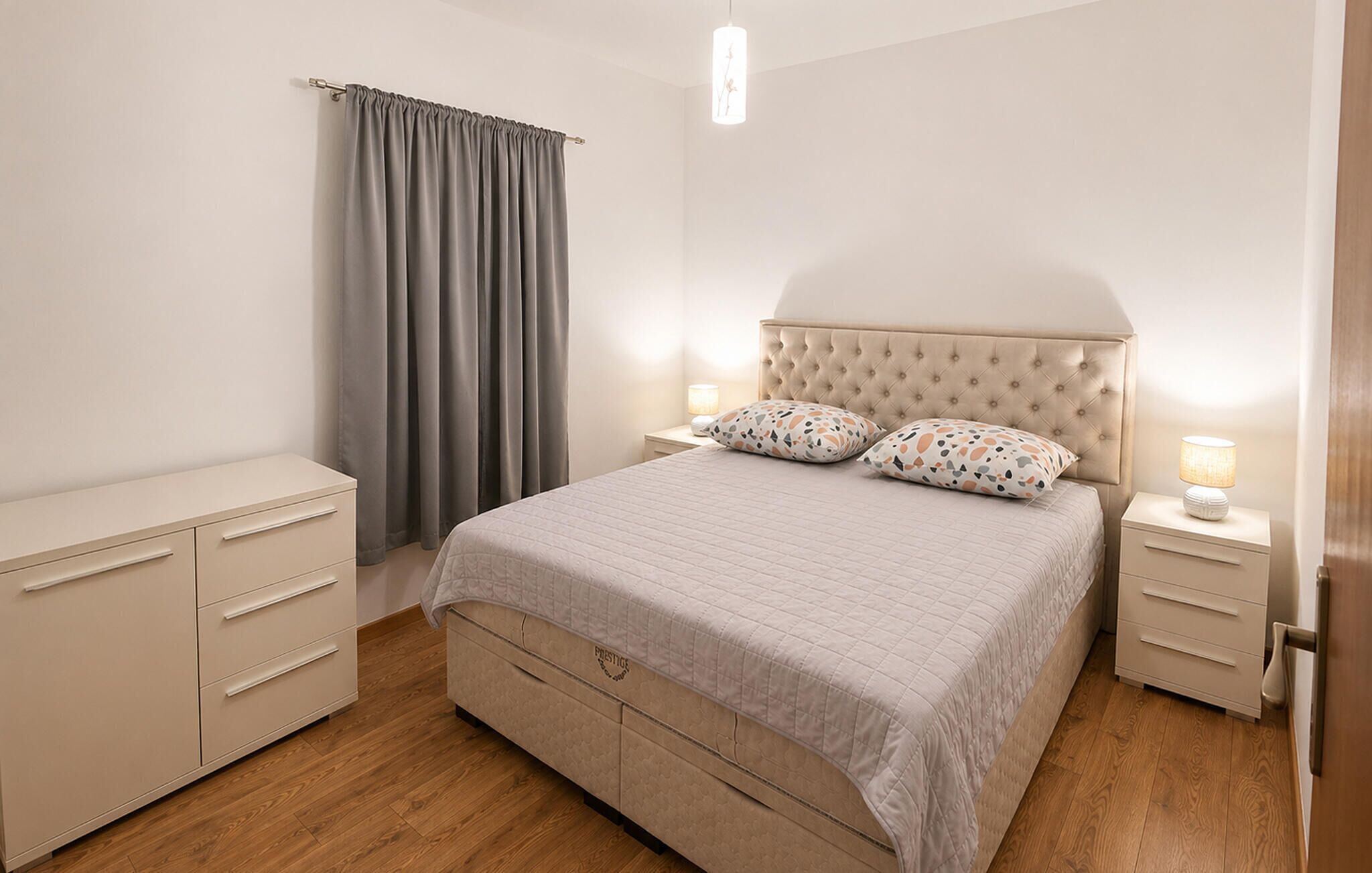 A bedroom with a bed, nightstands, a dresser, and a window with curtains.