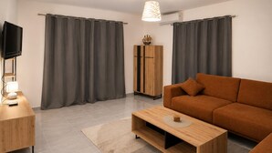 Ein modernes Wohnzimmer mit Sofa, Couchtisch, Fernseher und Vorhängen.