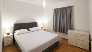 Ein ordentlich eingerichtetes Schlafzimmer mit Bett, Nachttischen, einem Kleiderschrank und einem Fenster mit Vorhängen.