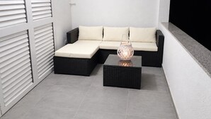 Ein modulares Sofa mit Kissen, zwei schwarze Rattan-Beistelltische und ein dekorativer Laternenleuchter.
