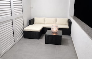 Ein modulares Sofa mit Kissen, zwei schwarze Rattan-Beistelltische und ein dekorativer Laternenleuchter.