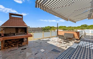Eine Dachterrasse mit gemauertem Grill, Sitzgelegenheiten im Freien und Blick auf Grünflächen.