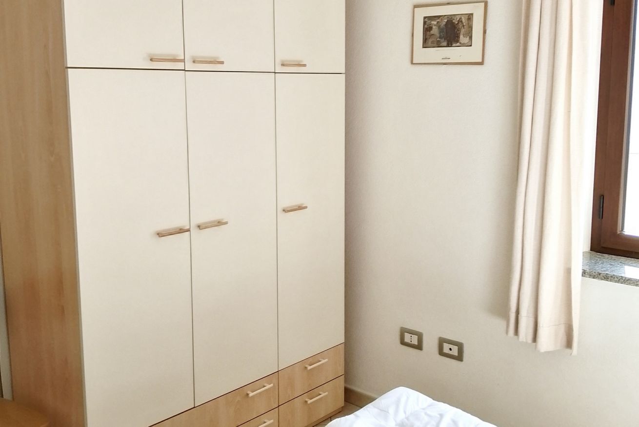 Ein Schlafzimmer mit Kleiderschrank, Bett, einem Fenster mit Vorhängen und einem an der Wand befestigten Lichtschalter.