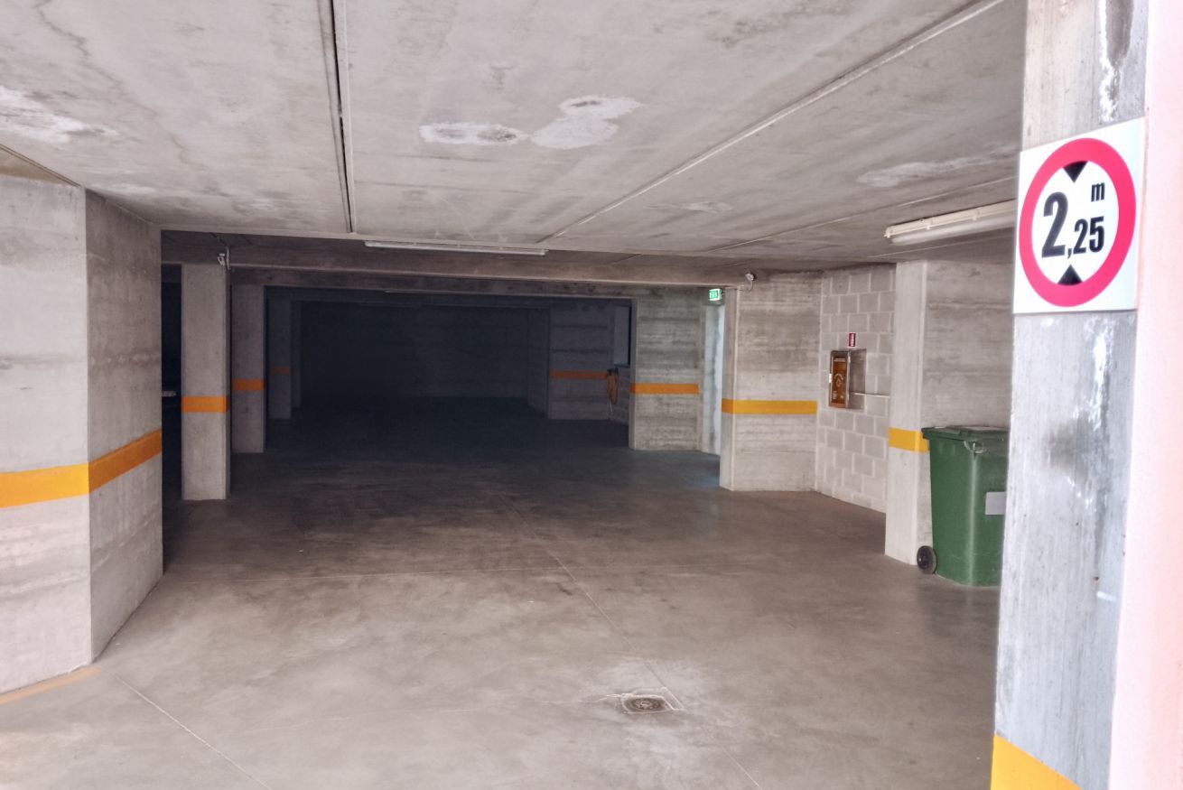 A parking garage with concrete pillars, a sign indicating a height limit of 2.25 meters, and a green trash bin.