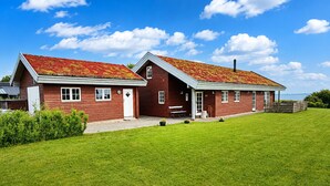 Ett tvåvåningshus byggt av trä, med ett rött tak, en veranda och en välskött gräsmatta.
