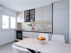 A modern kitchen with a built-in dishwasher, a sink, and a dining area with a table and chairs. - Apartman Dolce (Trpanj)