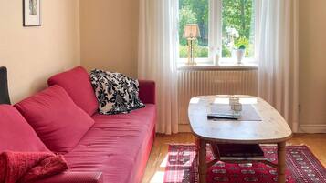 A room with a red sofa, a small table, a window with curtains, and a patterned rug.