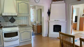 Une cuisine avec un poêle blanc, des armoires en bois, une cheminée et un coin repas comprenant une table et des chaises en bois.