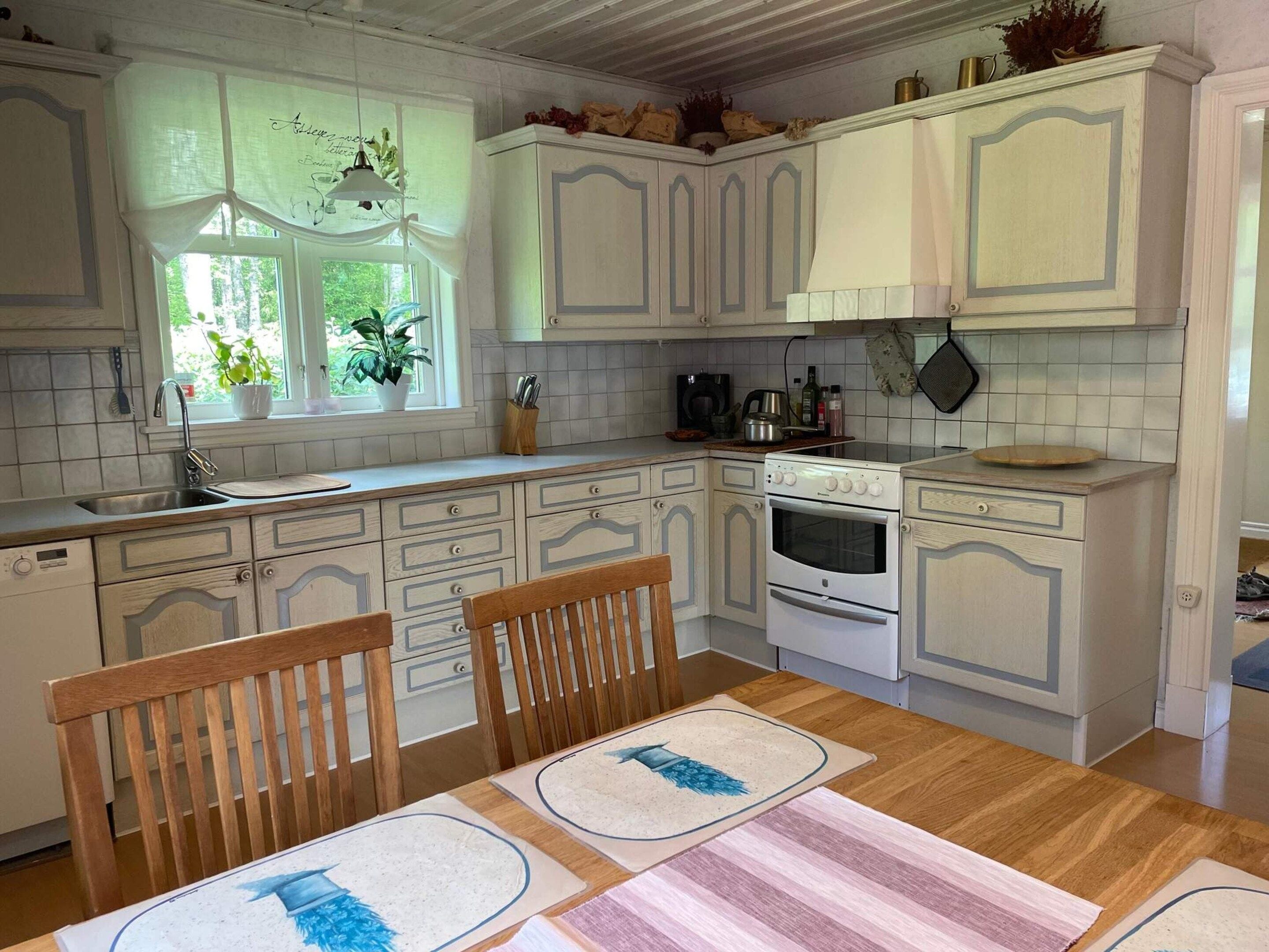 Una cocina con armarios blancos, una mesa de comedor de madera y una ventana con plantas.