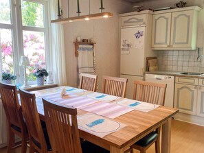 A dining area with a wooden table, chairs, and a window with potted plants. - 4 Star Holiday Home in Hindas (Hindas)