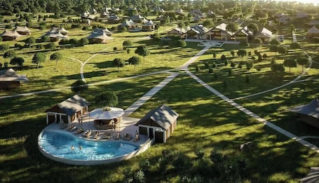 An aerial view of a resort with multiple thatched-roof cottages, a central swimming pool, and well-maintained lawns.