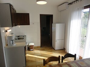 A compact kitchen with a sink, stove, and refrigerator, a dining table with chairs, and a view through a window with curtains. - Villa Matan (Murter-Kornati)