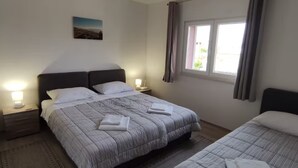 Una cama doble con un edredón a rayas, una mesita de noche con una lámpara, una ventana con cortinas y un cuadro en la pared.