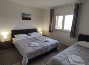 Ein Doppelbett mit gestreifter Bettdecke, ein Nachttisch mit Lampe, ein Fenster mit Vorhängen und ein Gemälde an der Wand.
