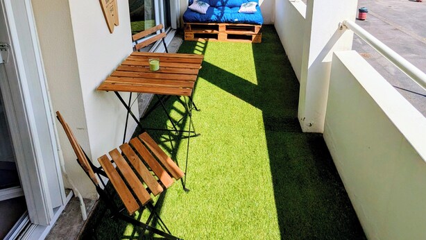 En balkon med blå sofa, træstole og et bord med en drik.