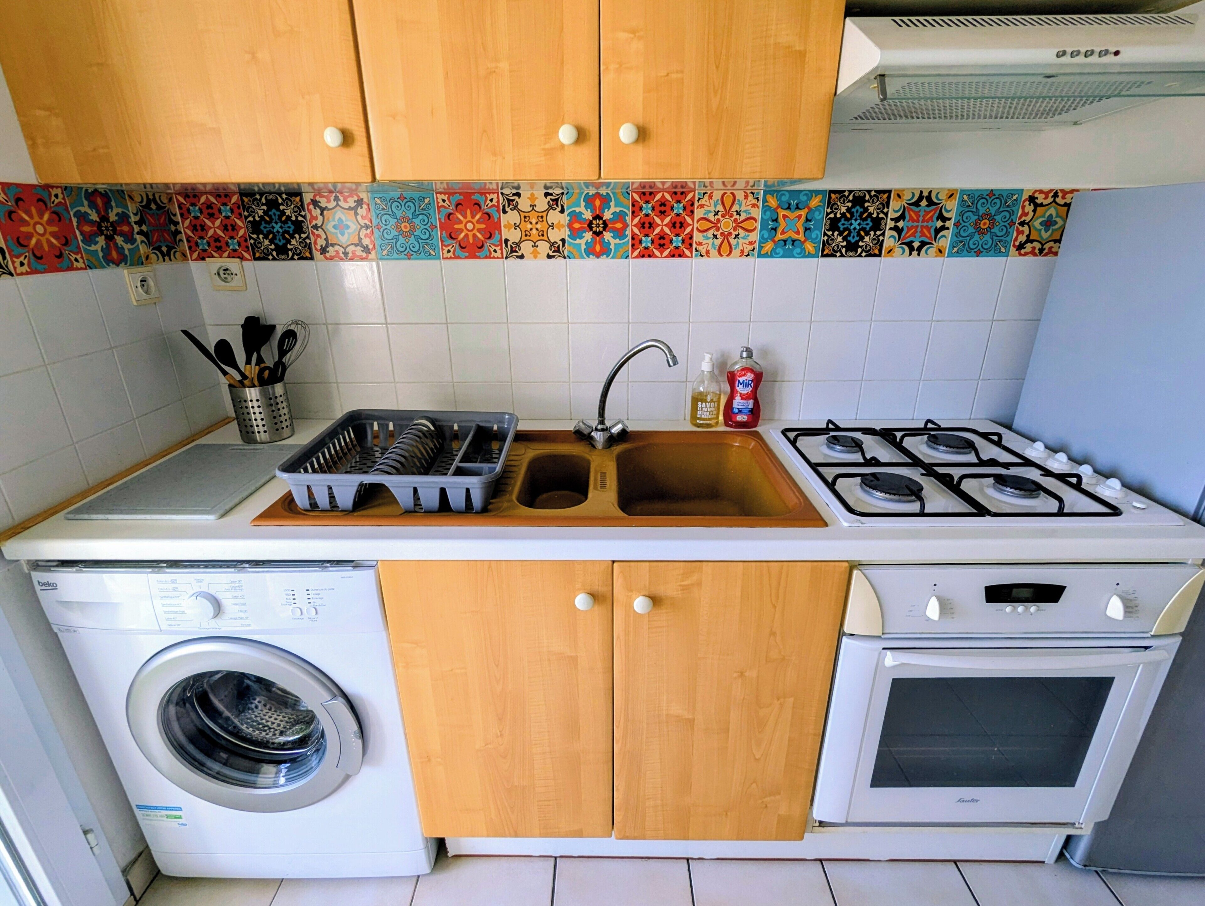Eine kleine Küche mit Waschmaschine, Spüle, Herd und Holzschränken.