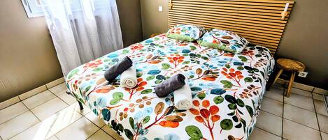 A neatly made bed with a floral bedspread, a wooden headboard, and a small stool beside it.
