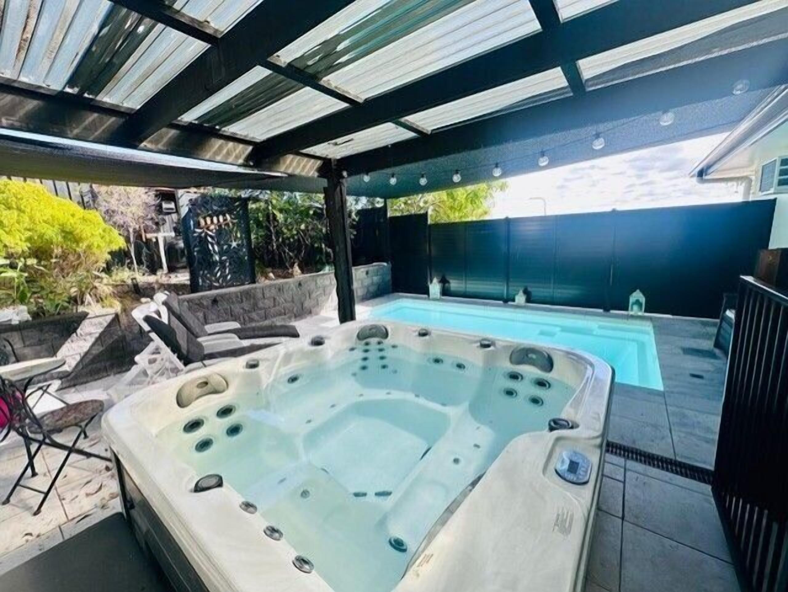 Un bain à remous avec une terrasse carrelée, une piscine et un espace patio couvert.