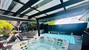 Un jacuzzi con plataforma de azulejos, una piscina y un patio cubierto.