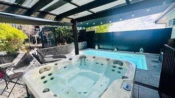 A hot tub with a tiled deck, a pool, and a covered patio area.