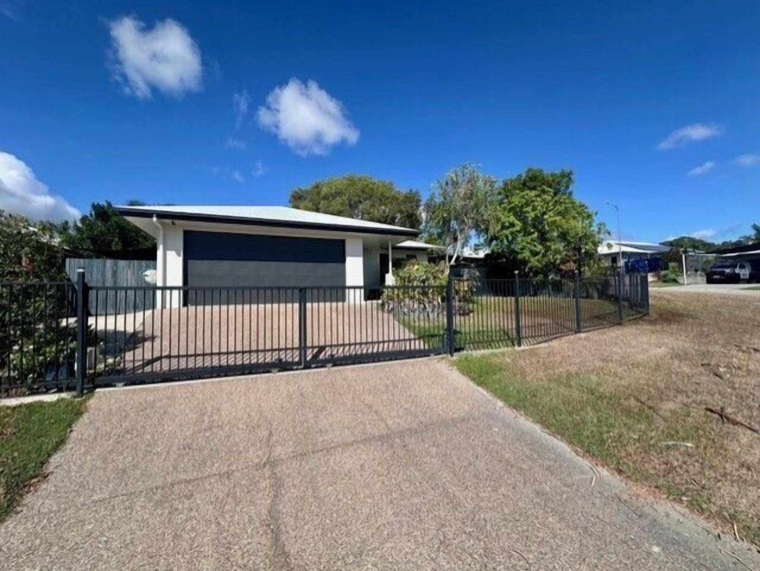 A modern two-story house with a garage, a paved driveway, and a black metal fence.