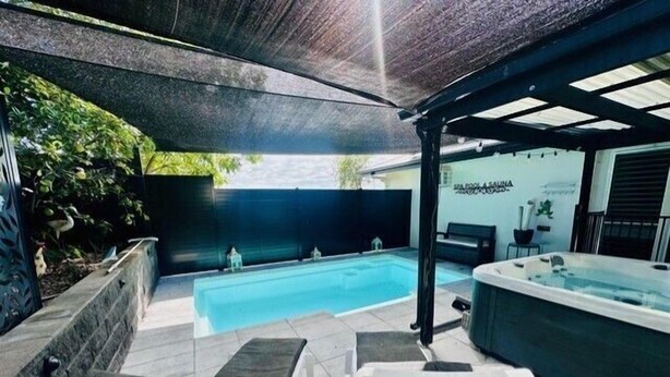 Un área de piscina con un jacuzzi, dos sillas reclinables y una zona de estar cubierta.