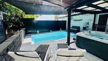 A pool area with a hot tub, two lounge chairs, and a covered seating area.