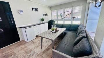 A compact living space with a kitchenette, a dining table, a sofa, and a small refrigerator.