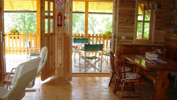 A wooden cabin interior with a dining area, a chair, a table, and a view of the outside.