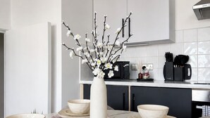 Uma cozinha moderna com armários brancos, um exaustor Bosch e um vaso com galhos e flores brancas sobre a mesa de mármore.