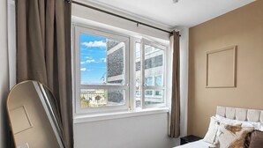 Um quarto com cama, janela, espelho e lustre.