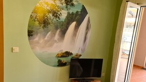 Ein Wohnzimmer mit einer großen Wandmalerei eines Wasserfalls, einem Fernseher auf einer Holzkommode und einer Glastür, die zu einem Außenbereich führt.