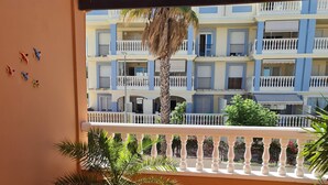 Ein Balkon mit Stuhl, Topfpflanzen und Blick auf ein mehrstöckiges Gebäude mit Balkonen.