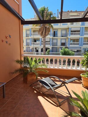 Ein Balkon mit Stuhl, Topfpflanzen und Blick auf ein mehrstöckiges Gebäude mit Balkonen.