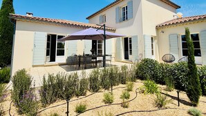 Ein zweigeschossiges Haus mit Terrasse, Sitzgelegenheiten im Freien und einem Garten.