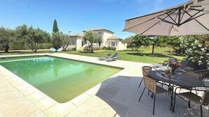 Ein Swimmingpool mit Liegestühlen und einem Sonnenschirm, umgeben von einem Garten und einem Gebäude.