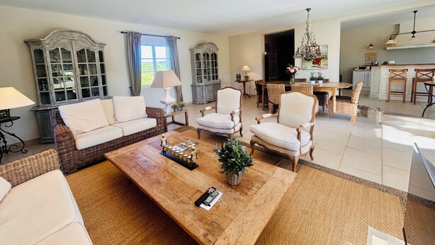 Ein geräumiges Wohnzimmer mit einem großen Couchtisch aus Holz, Korbsesseln und einem Essbereich mit Holztisch und Stühlen.
