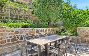 An outdoor patio with a stone wall, a table, and chairs. - Beautiful apartment in Obrovac with WiFi (Obrovac)