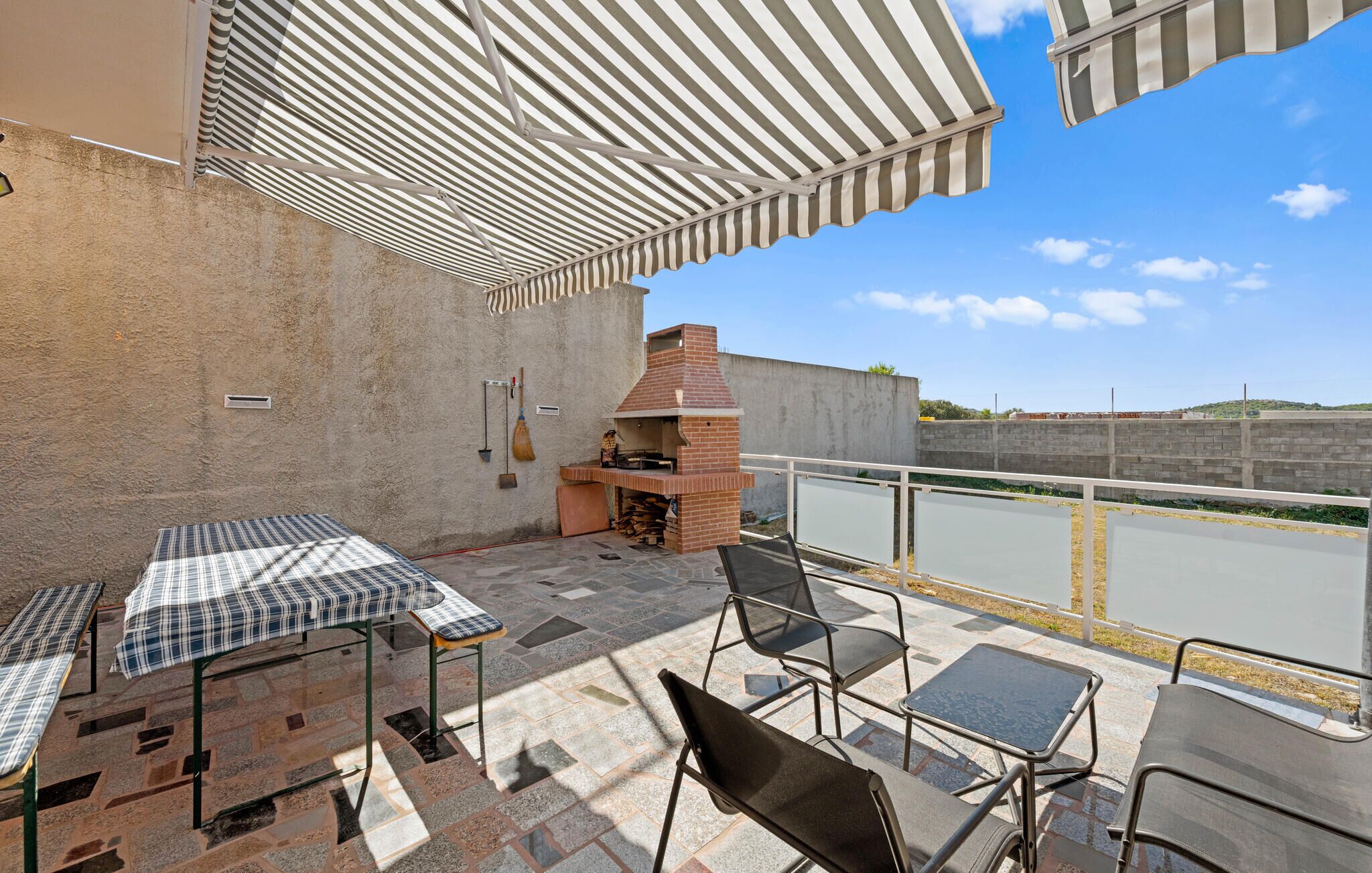 Une terrasse extérieure dotée d’un barbecue en briques, de stores rayés et offrant une vue sur un paysage lointain.