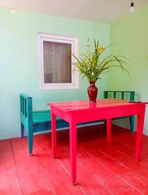 A room with a red table, a window with a curtain, a vase with flowers, and a green chair.