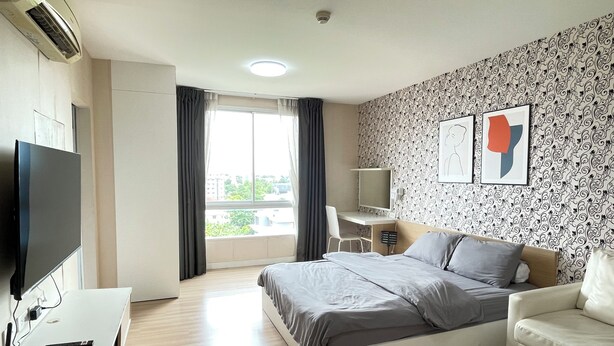 A hotel room with a bed, a desk, a TV, a chair, and a window with curtains. - Room117atchangwattana (Pak Kret)