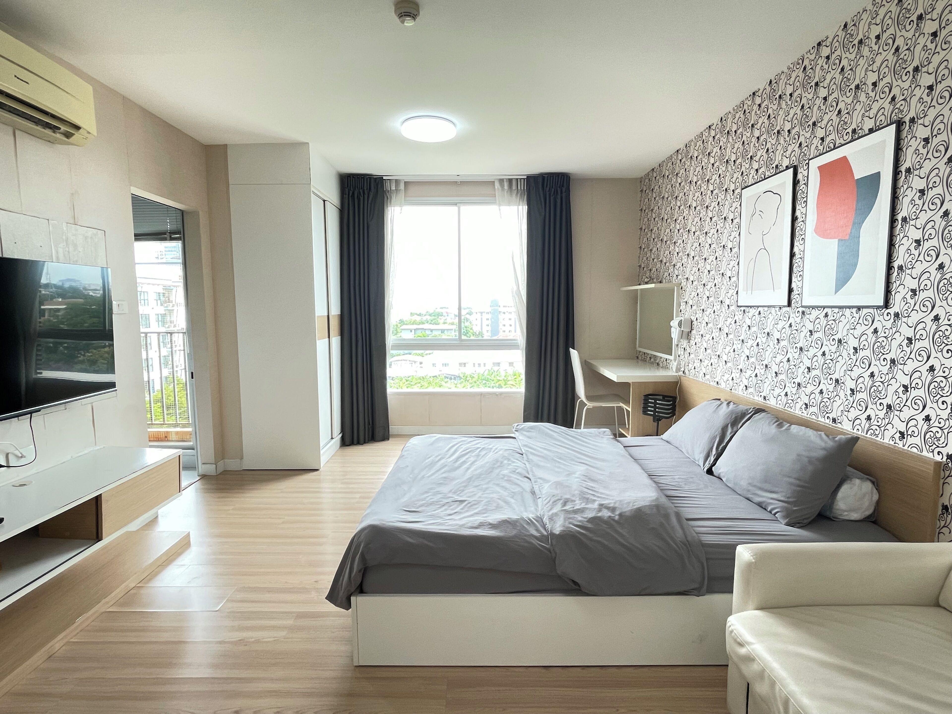 A modern hotel room with a bed, a desk, a TV, and a balcony with curtains.
